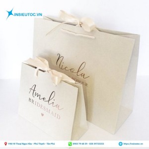 Túi giấy đựng quà nền trắng gắn nơ in tên thương hiệu nổi bật sang trọng. Túi giấy đựng quà nền trắng